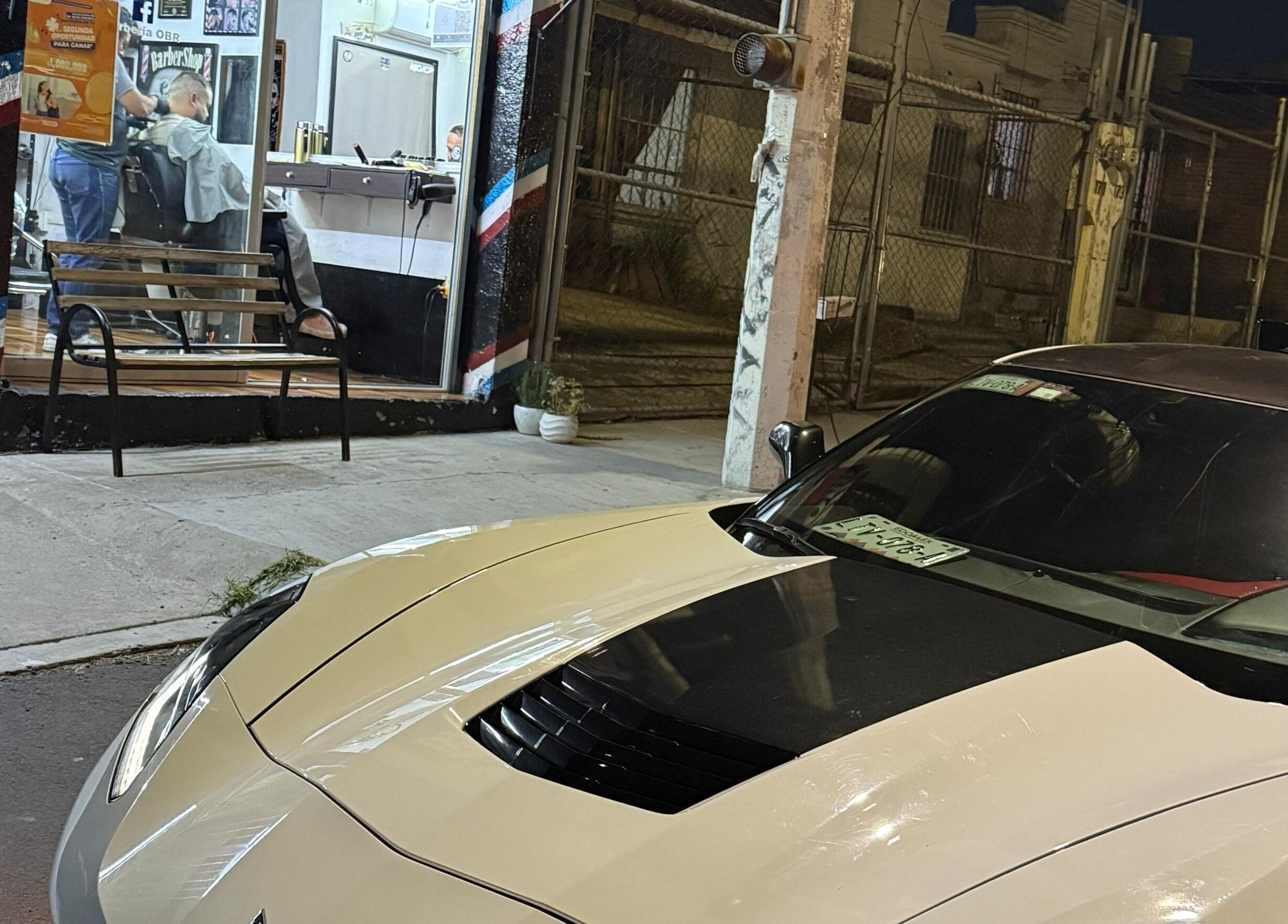 Exterior nocturno de Barberia OBR en Santiago De Querétaro, MX con auto estacionado al frente.