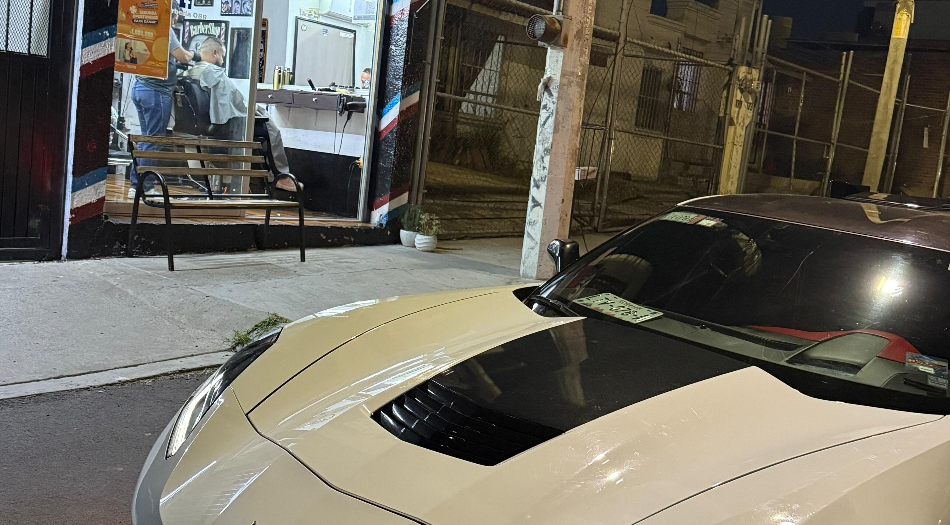 Exterior nocturno de Barberia OBR en Santiago De Querétaro, MX con auto estacionado al frente.