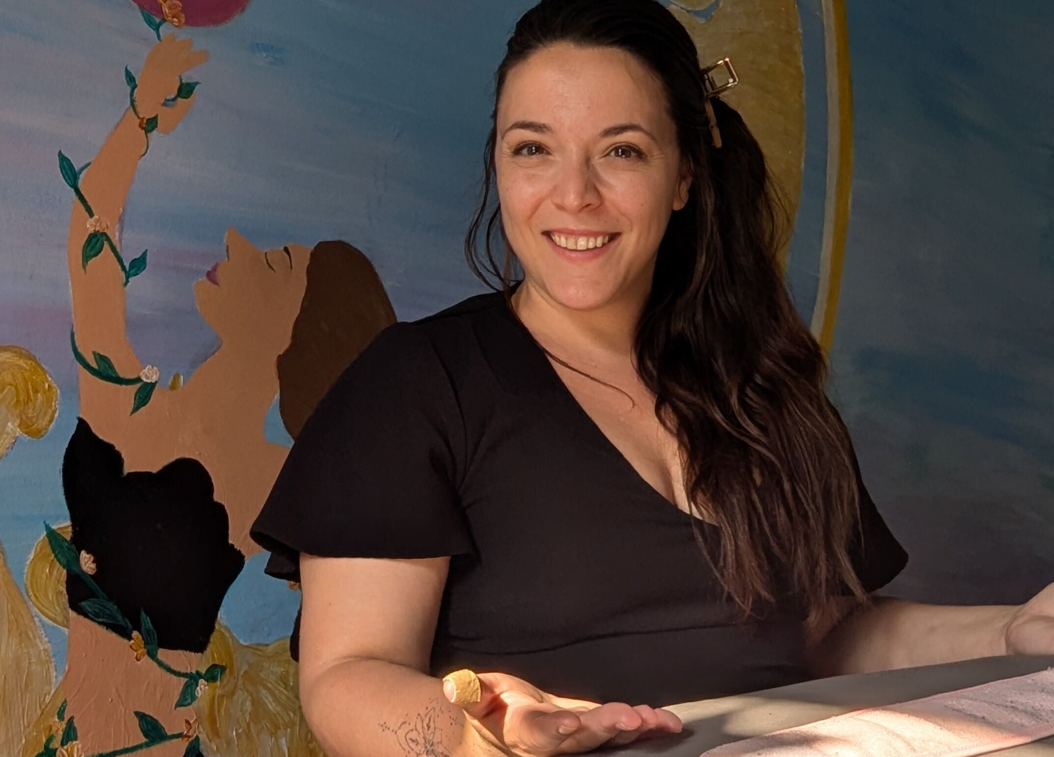 Visage souriant chez l'Alchimie de la beauté, Montréal, Québec, CA avec une fresque inspirante en arrière-plan.