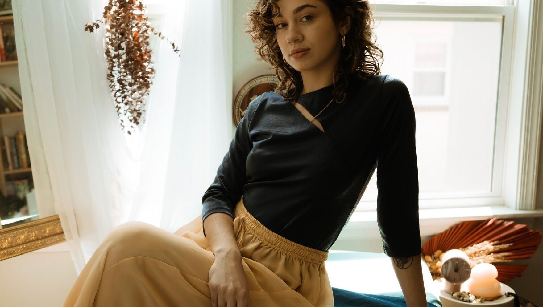 A serene woman at Hands of Chiron, Baltimore, Maryland, US, relaxing in a sunlit room adorned with dried plants.