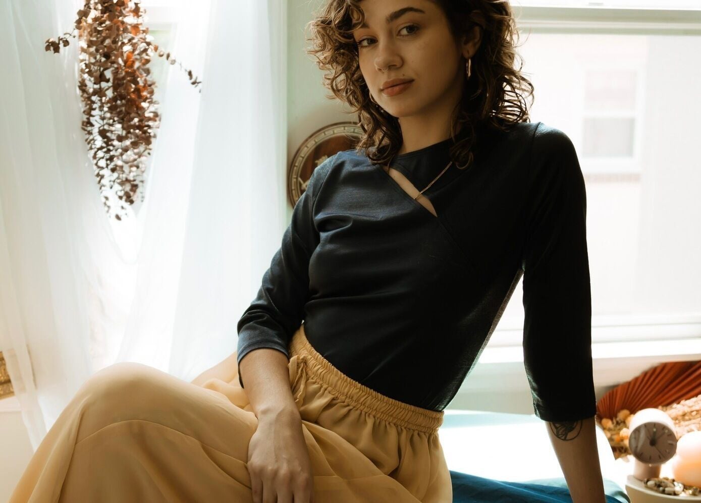 A serene woman at Hands of Chiron, Baltimore, Maryland, US, relaxing in a sunlit room adorned with dried plants.
