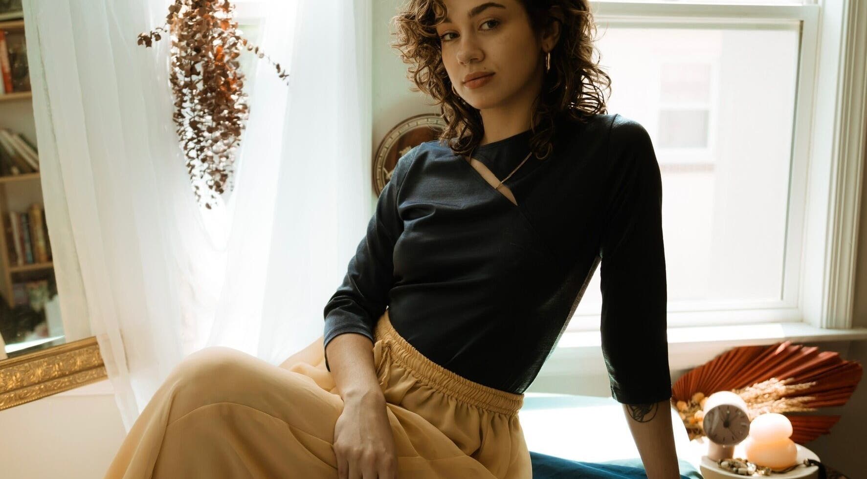 A serene woman at Hands of Chiron, Baltimore, Maryland, US, relaxing in a sunlit room adorned with dried plants.