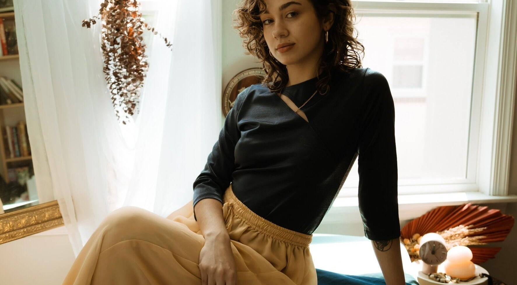 A serene woman at Hands of Chiron, Baltimore, Maryland, US, relaxing in a sunlit room adorned with dried plants.