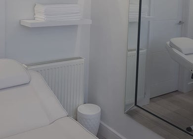 Calming treatment room at Sculpted & Skin, Ware, England, GB with a white massage bed and neatly stacked towels.