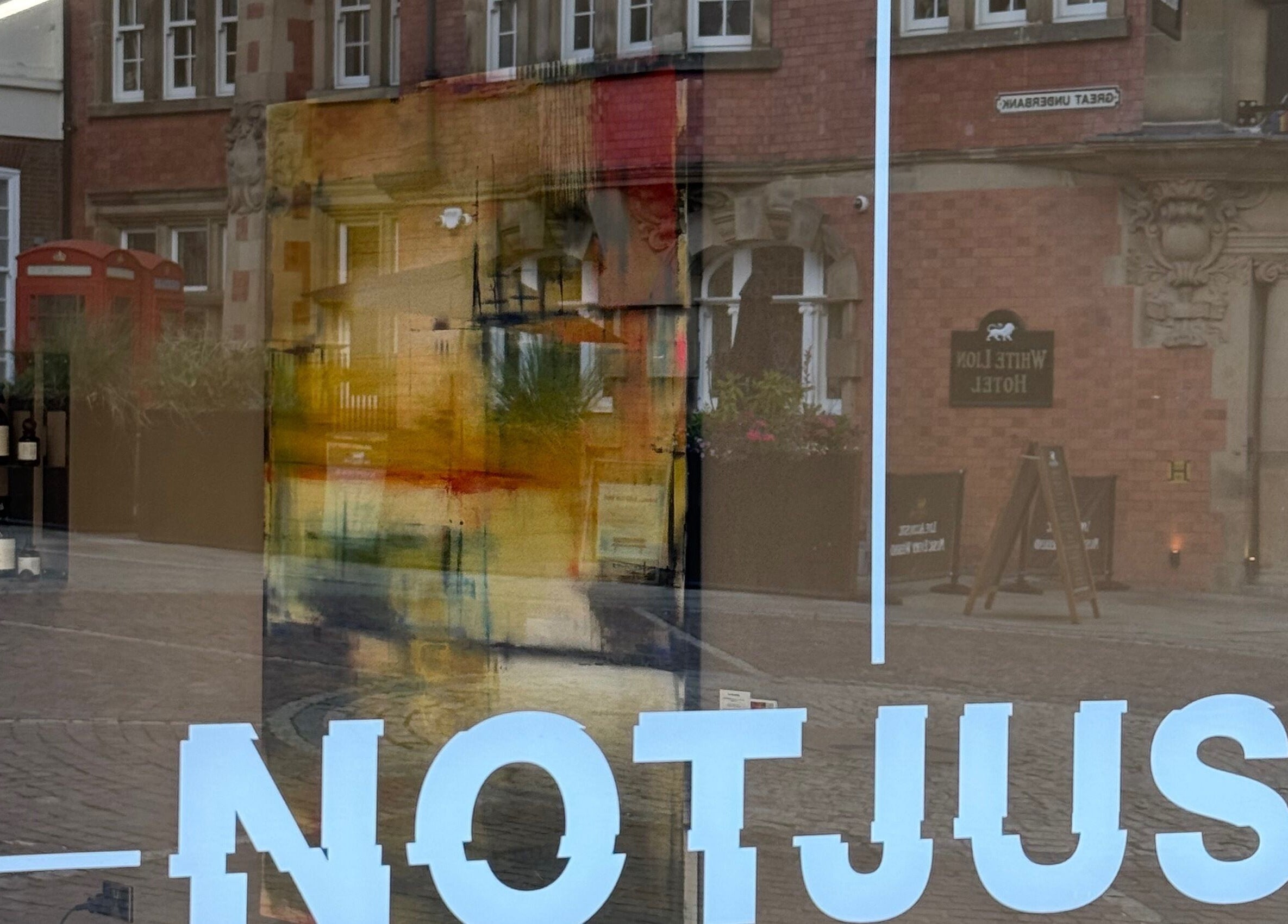 Reflection of NOTJUST - Stockport - The Underbanks with vibrant art in Stockport, England, GB window display.