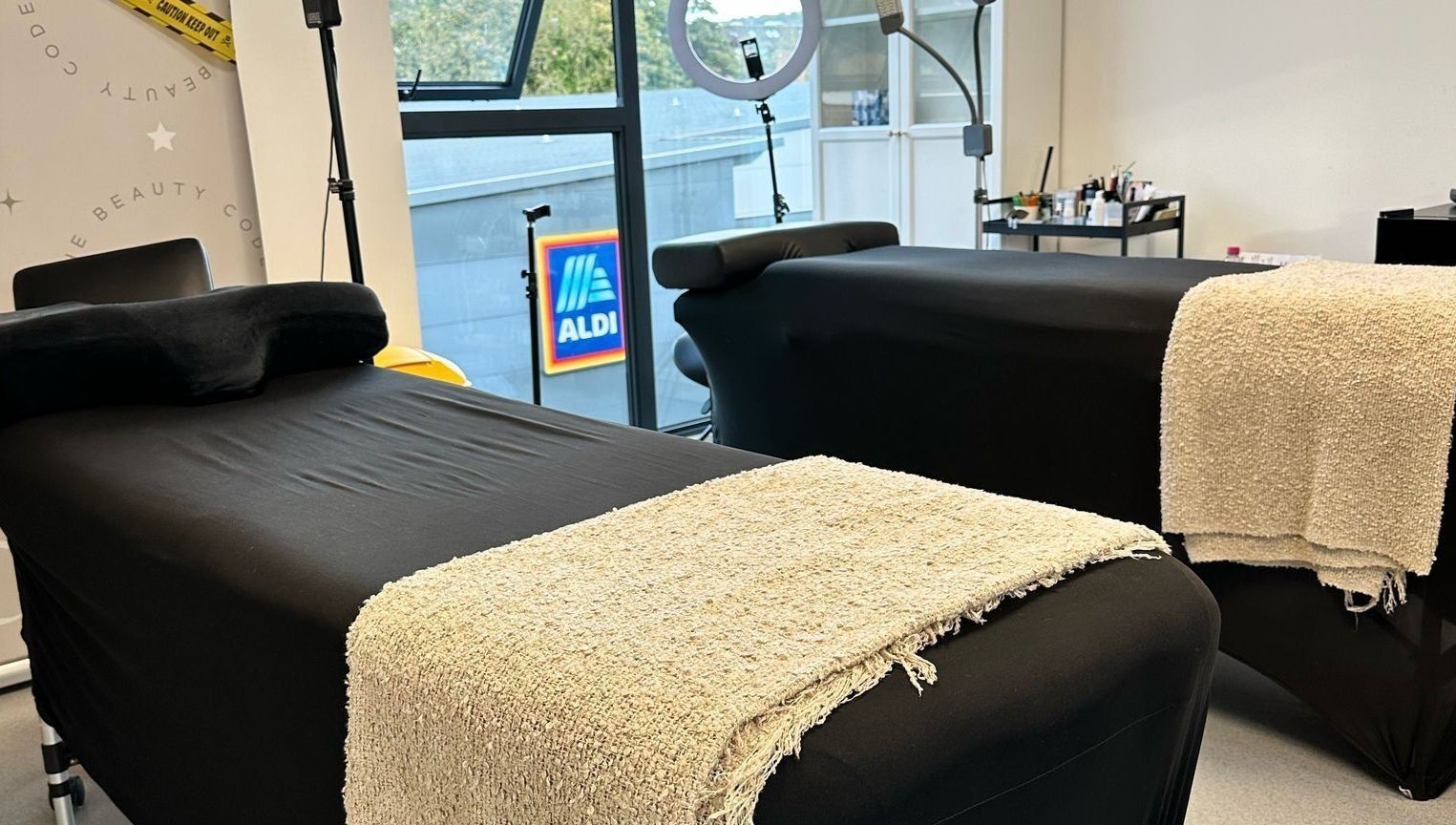 Two black spa beds with beige towels at Millzbeauty, High Wycombe, England, GB, near a large window.