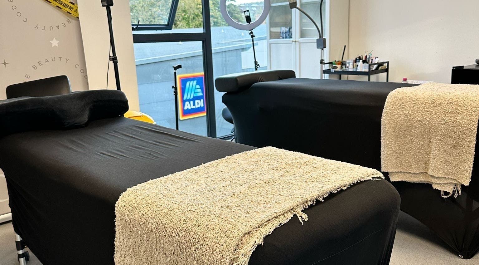 Two black spa beds with beige towels at Millzbeauty, High Wycombe, England, GB, near a large window.