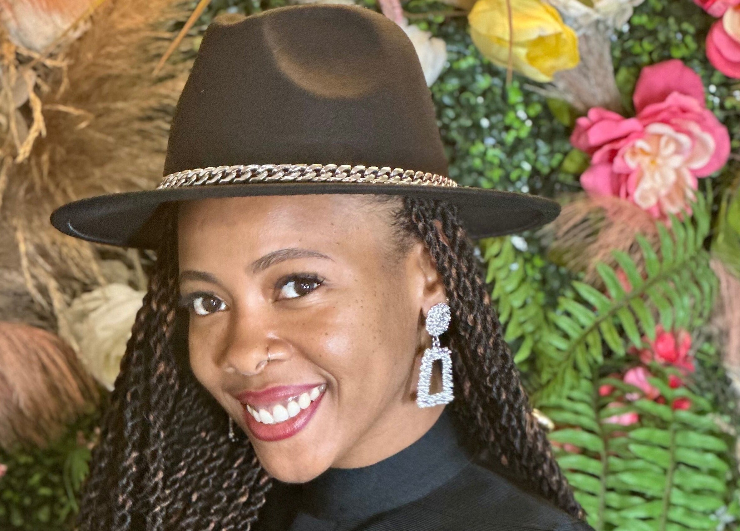 Smiling woman with hat at Black Oasis Luxury Mind & Body, Conyers, Georgia, US, surrounded by vibrant flowers.