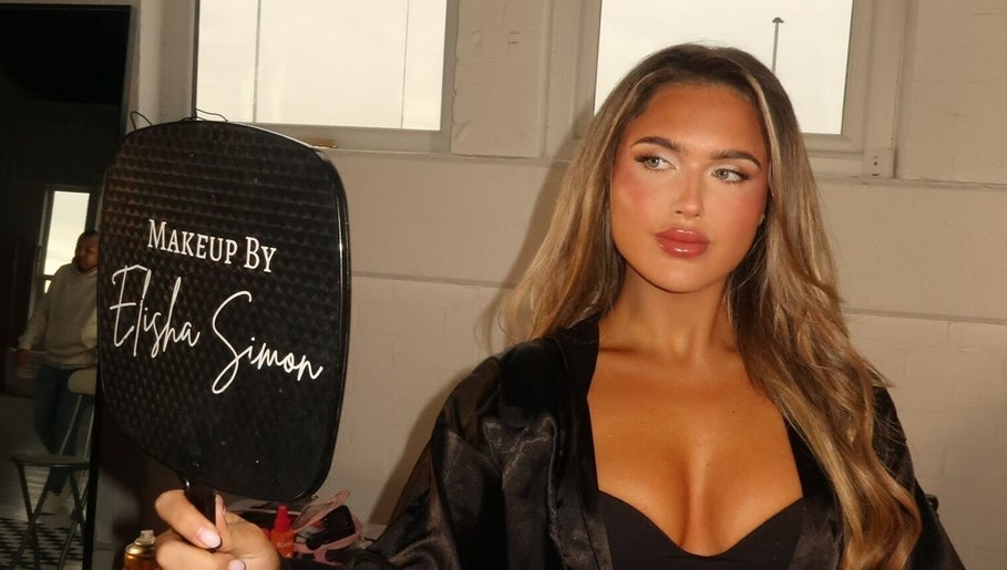 Woman holding mirror with 'Makeup by Elisha Simon' in Northampton, England, GB showcasing exquisite makeup.