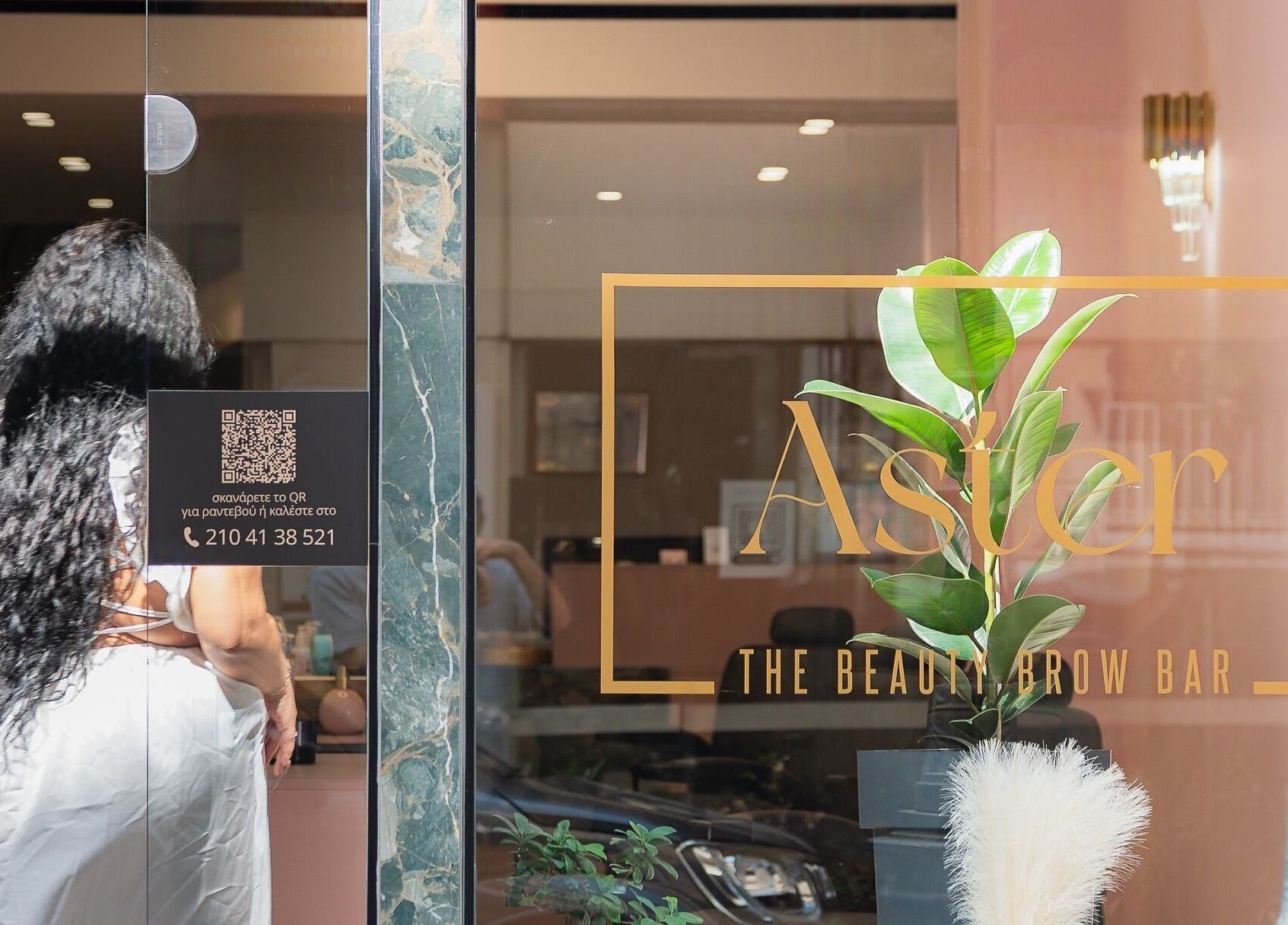 Είσοδος του Aster The Beauty Brow Bar στην Πειραιάς, GR, με φυτά και κομψή διακόσμηση.
