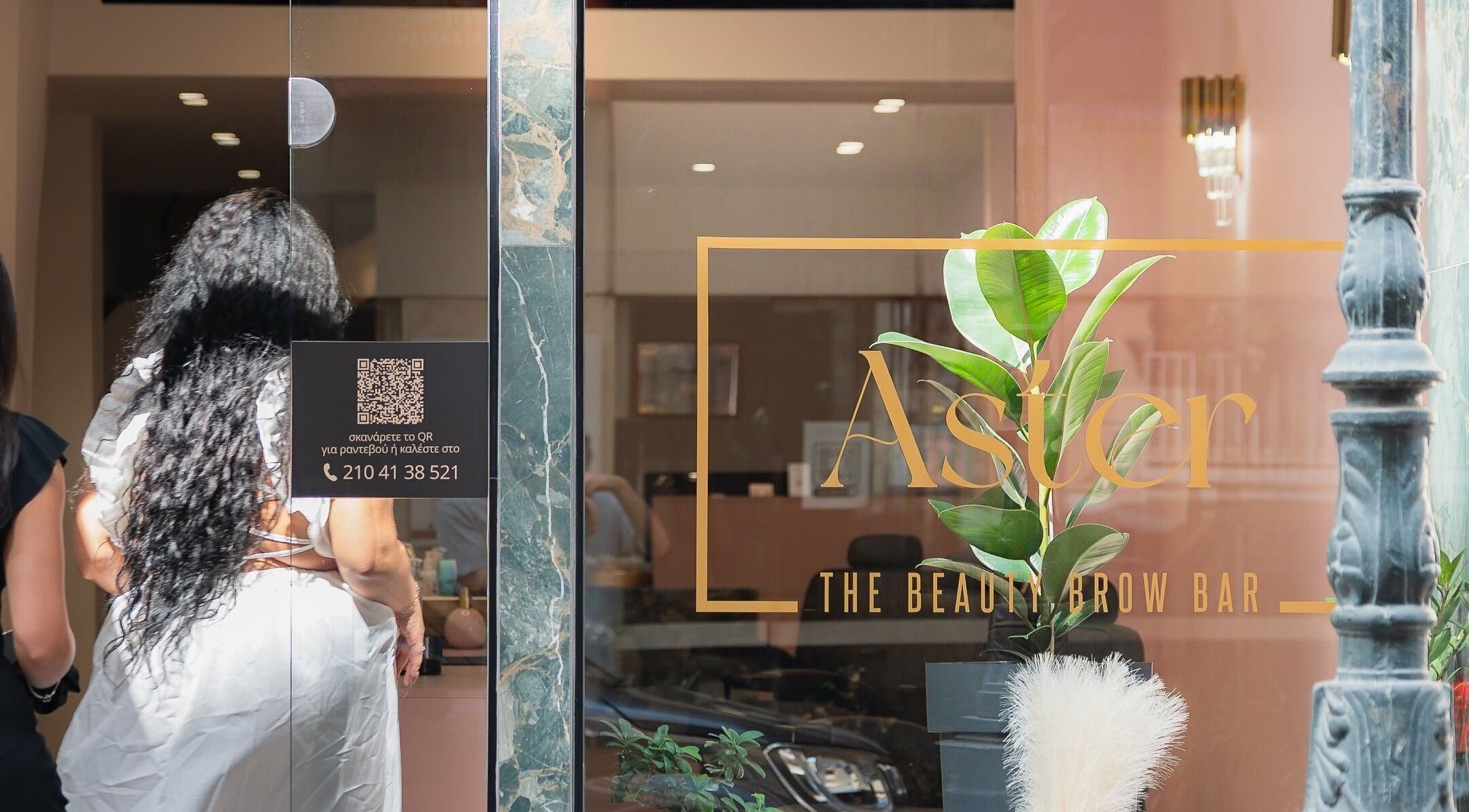 Είσοδος του Aster The Beauty Brow Bar στην Πειραιάς, GR, με φυτά και κομψή διακόσμηση.