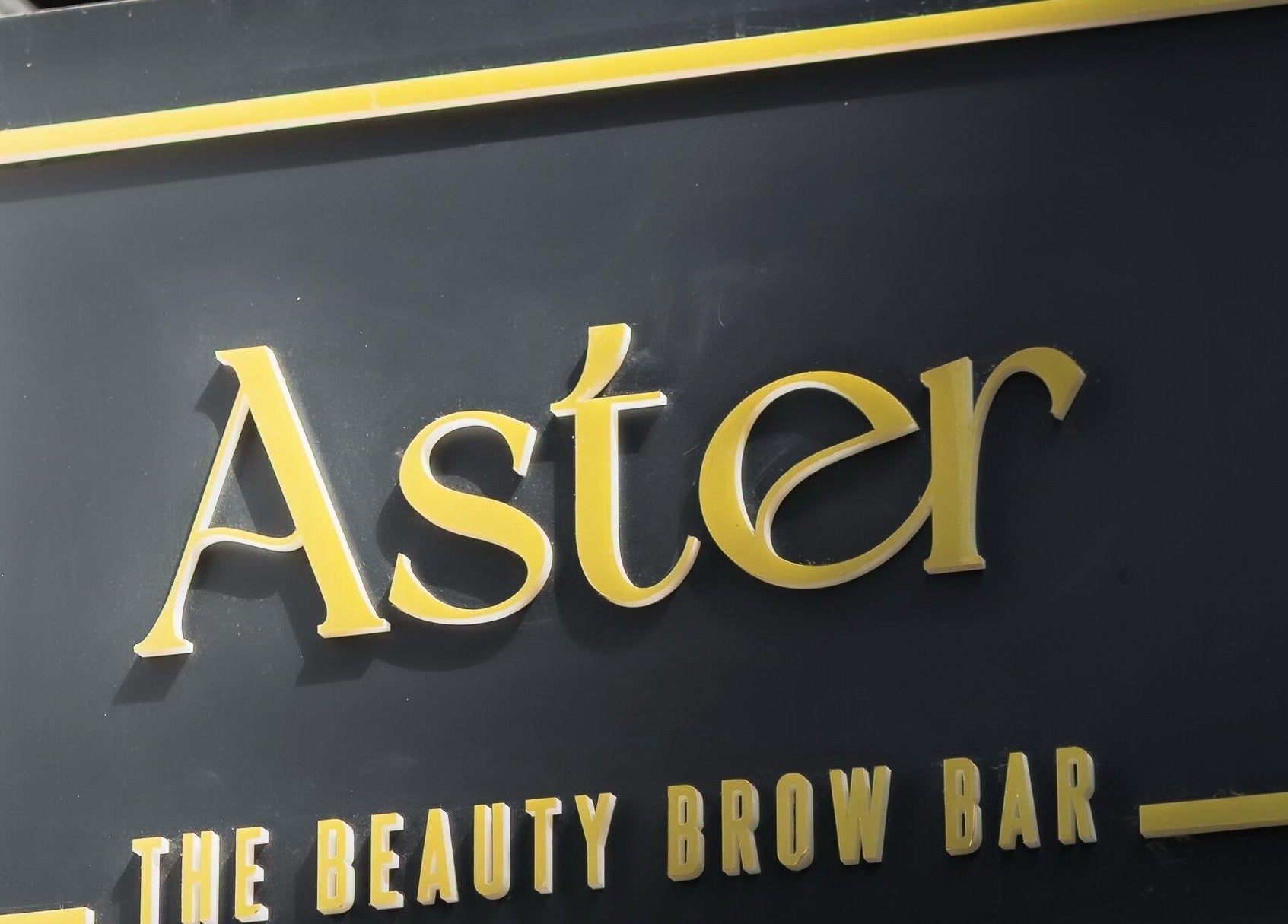 Πινακίδα του Aster The Beauty Brow Bar στην Πειραιά, GR με χρυσά γράμματα.