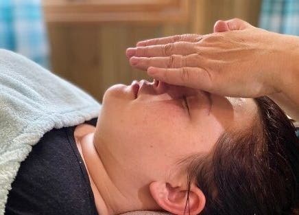 Relaxing therapy session at Wyrd Thistle Therapies, Methil, Scotland, GB. Hands placed gently on client's forehead.