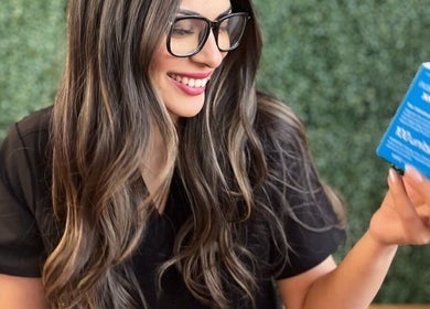 Smiling woman with long hair holding a product at Shine Beauty and Wellness, Overland Park, Kansas, US.