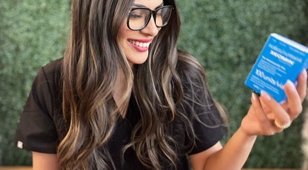 Smiling woman with long hair holding a product at Shine Beauty and Wellness, Overland Park, Kansas, US.