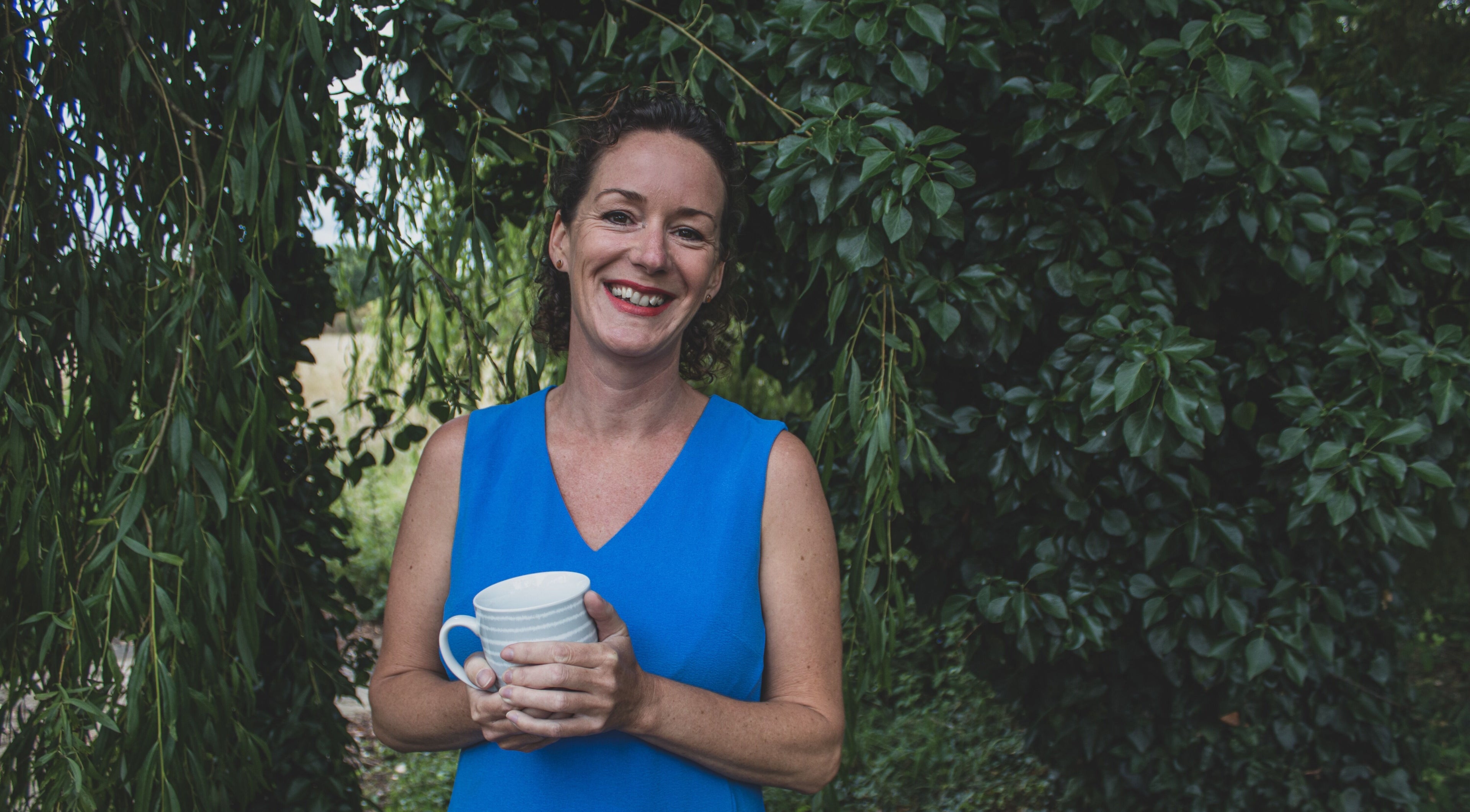 Smiling person holding a mug in lush garden at Amanda Smith Holistics - Framlingham, Framlingham, England, GB.