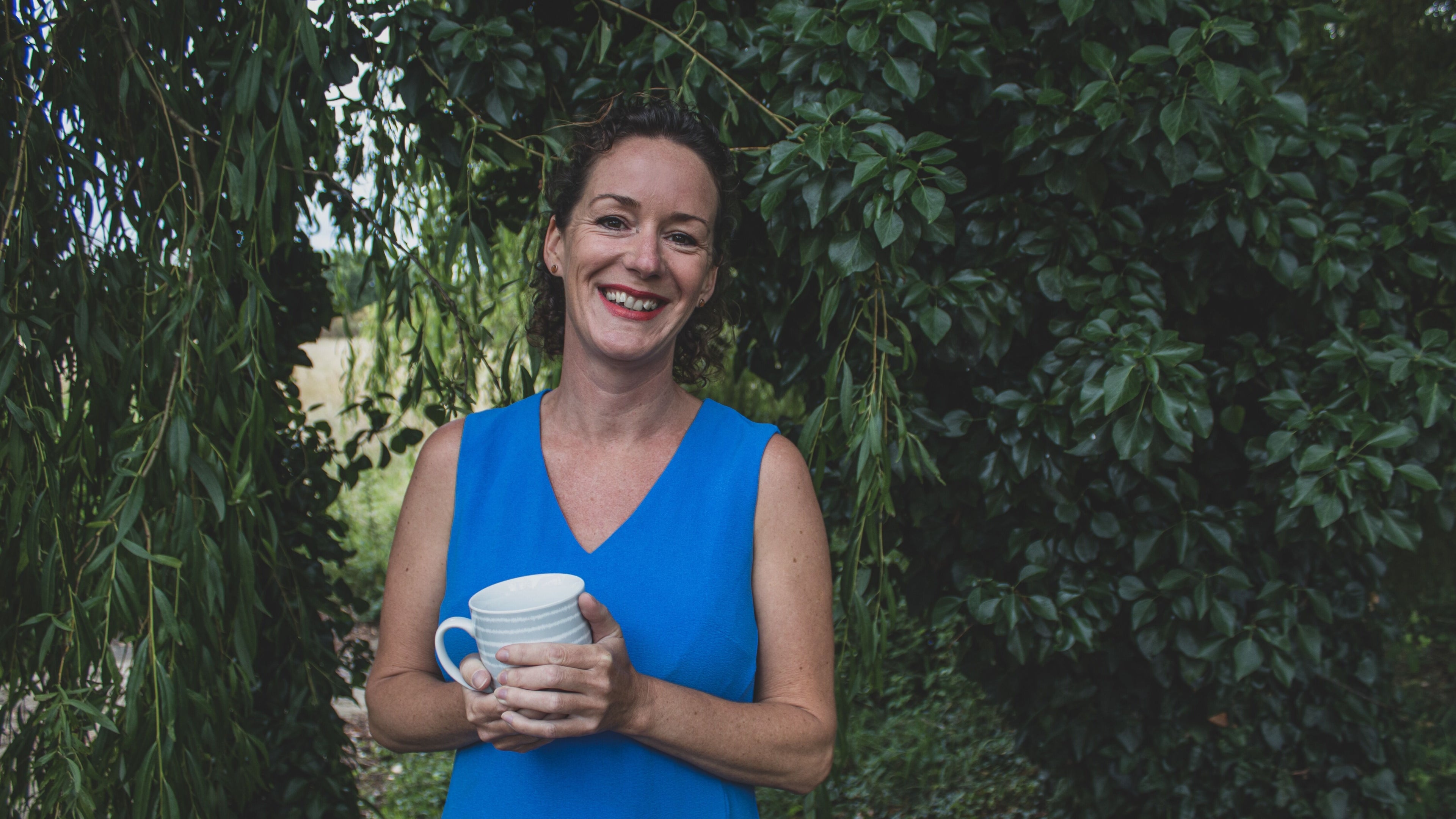 Smiling person holding a mug in lush garden at Amanda Smith Holistics - Framlingham, Framlingham, England, GB.