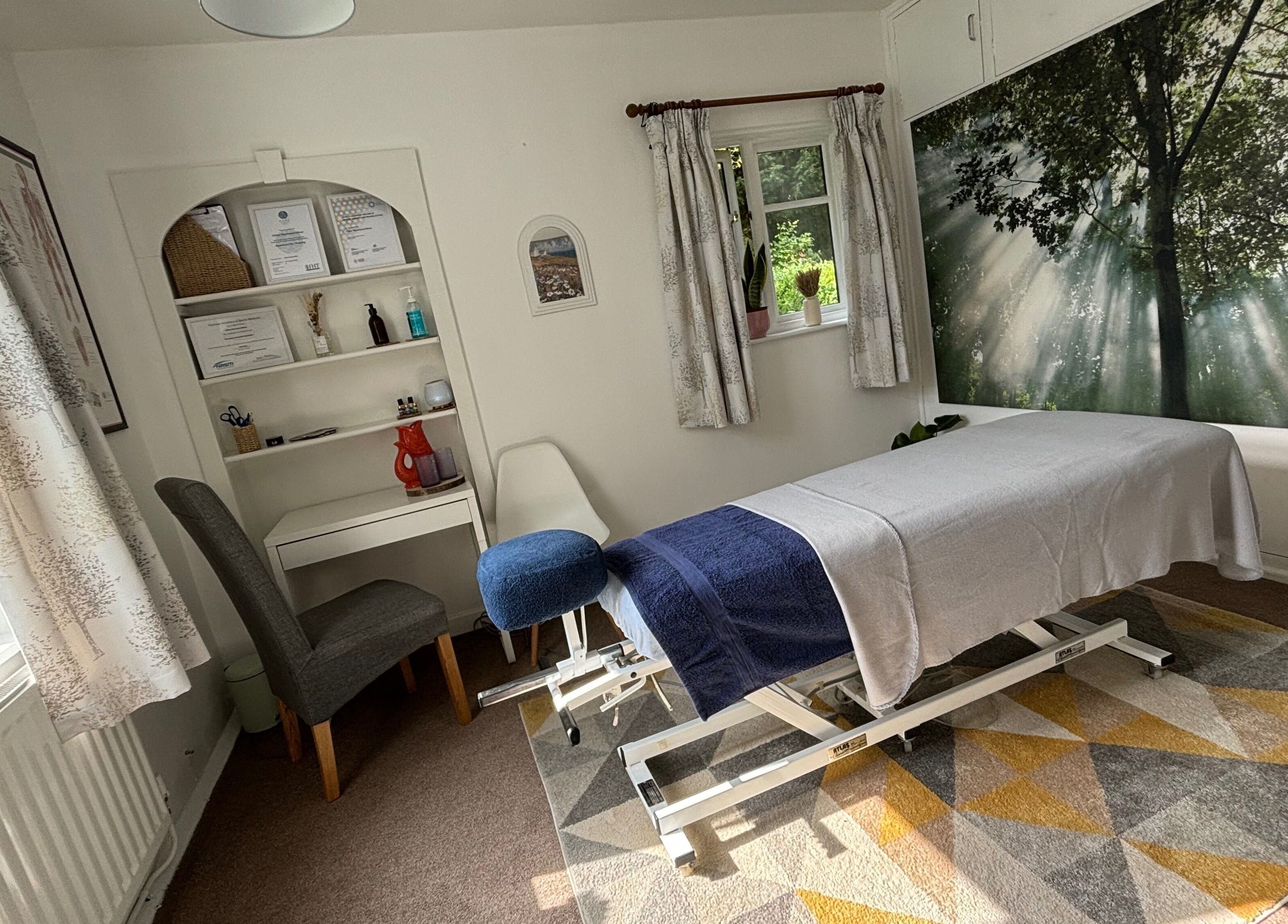Serene massage room at Rooted Wellness in Kineton, England, GB featuring a therapy bed and forest mural.