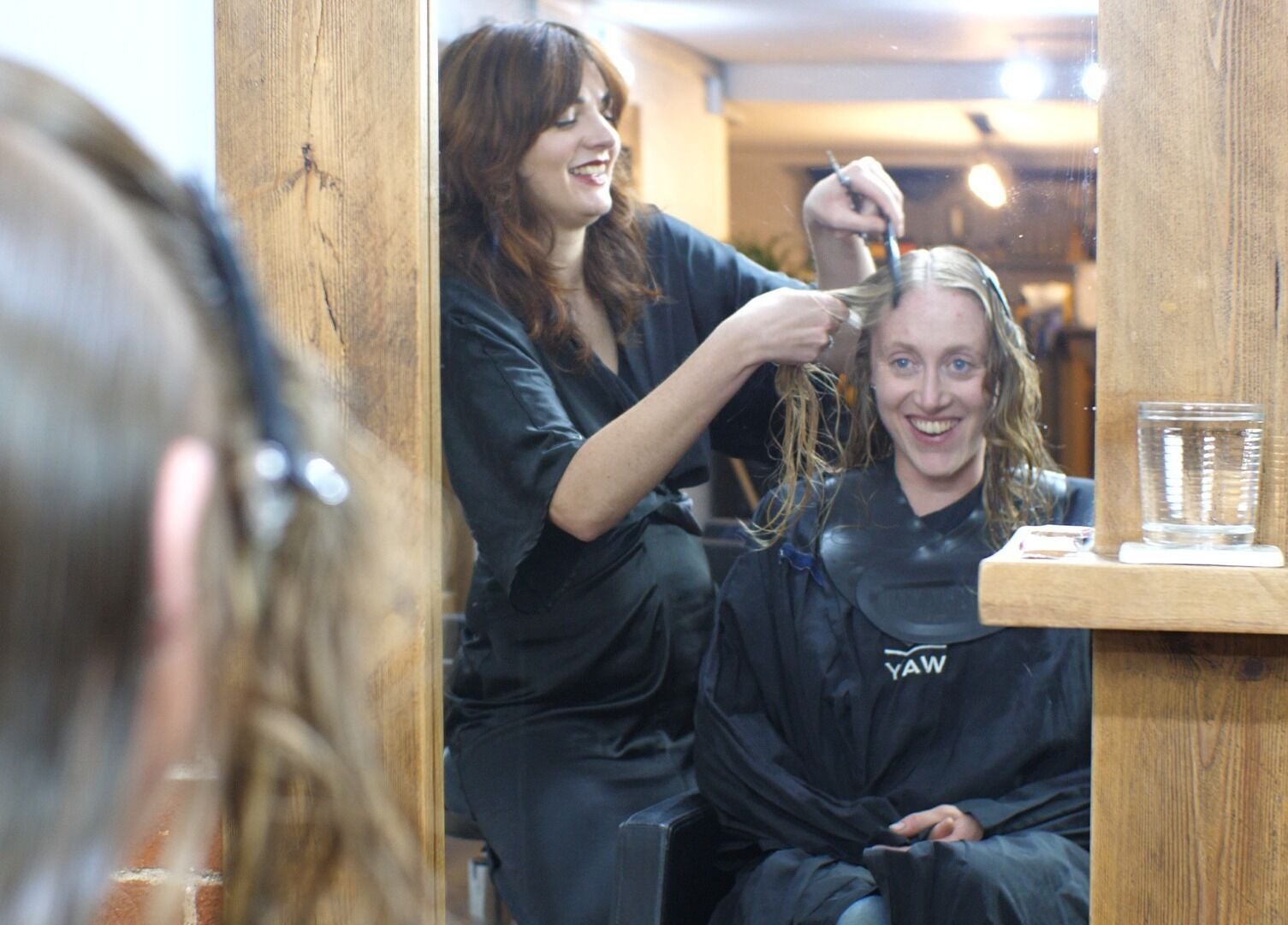 Stylist at Alice Capriotti, Lavenham, England, GB, expertly cutting client's hair with a smile.