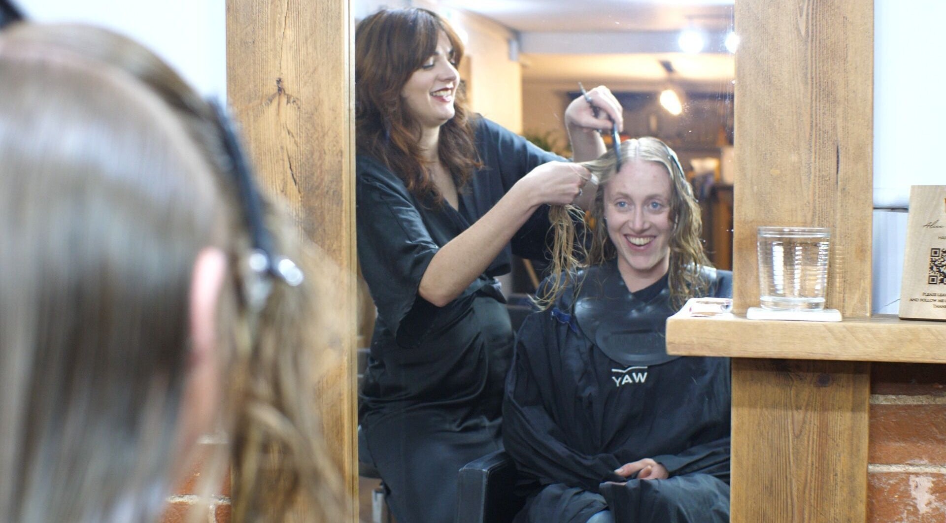 Stylist at Alice Capriotti, Lavenham, England, GB, expertly cutting client's hair with a smile.