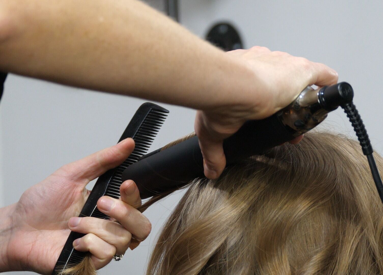 Hair styling at Alice Capriotti, Lavenham, England, GB showcasing expert techniques with a comb and curling iron.