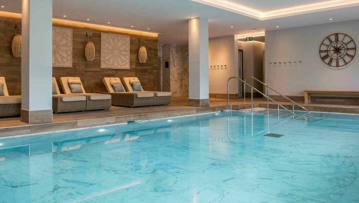 Luxurious indoor pool at The Hampton Spa in Failand, England, GB, featuring elegant loungers and soft lighting.