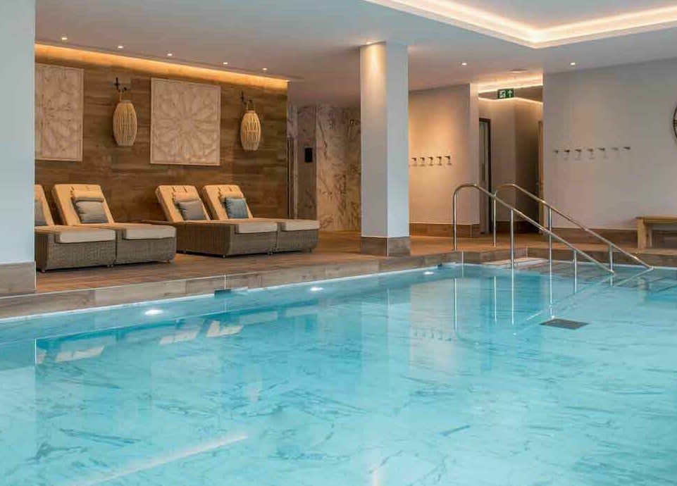 Luxurious indoor pool at The Hampton Spa in Failand, England, GB, featuring elegant loungers and soft lighting.