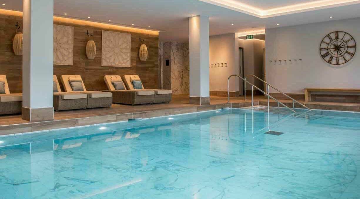 Luxurious indoor pool at The Hampton Spa in Failand, England, GB, featuring elegant loungers and soft lighting.