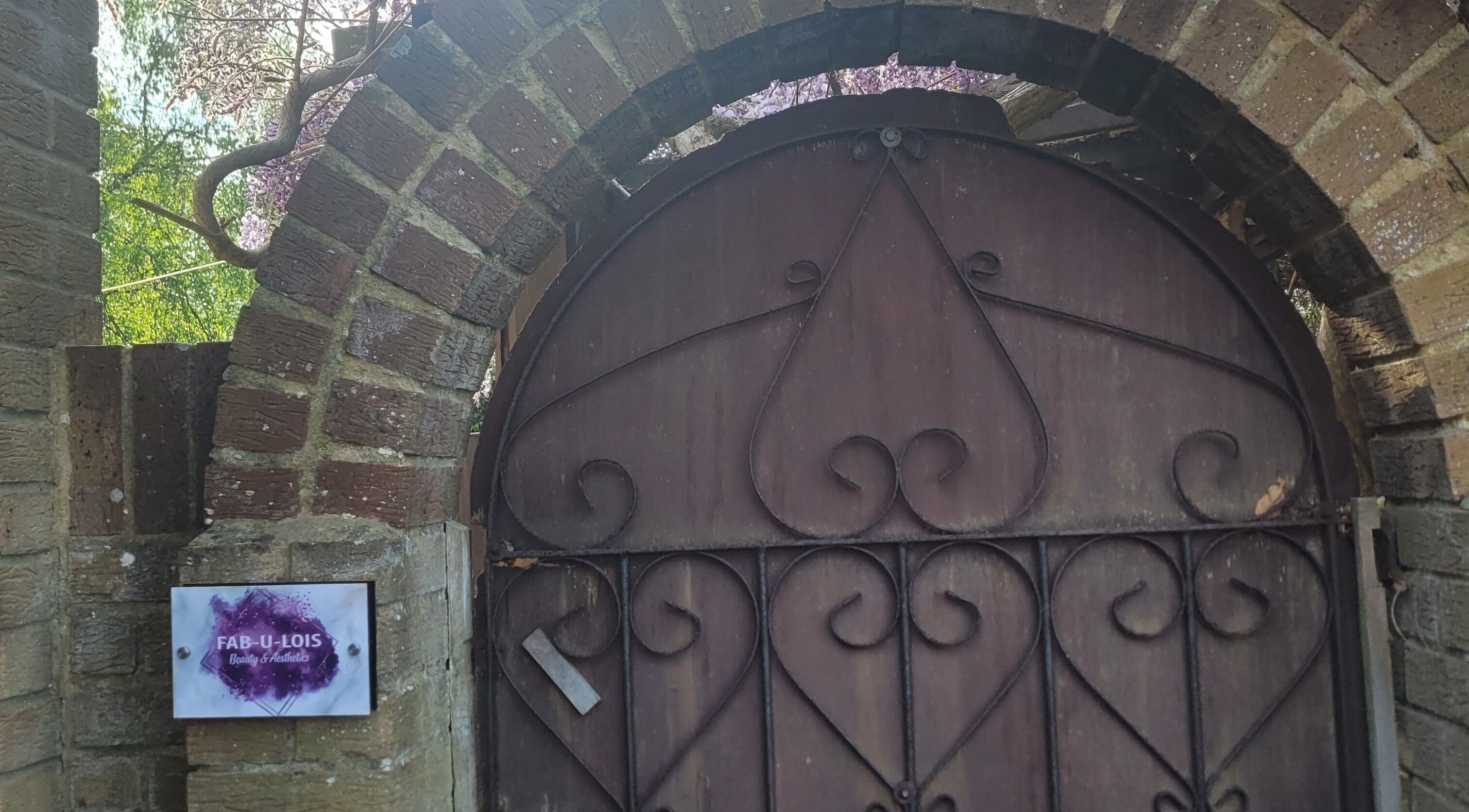 Rustic entry gate at Fab U Lois Beauty & Aesthetics in Rustington, England, GB, under a brick archway.