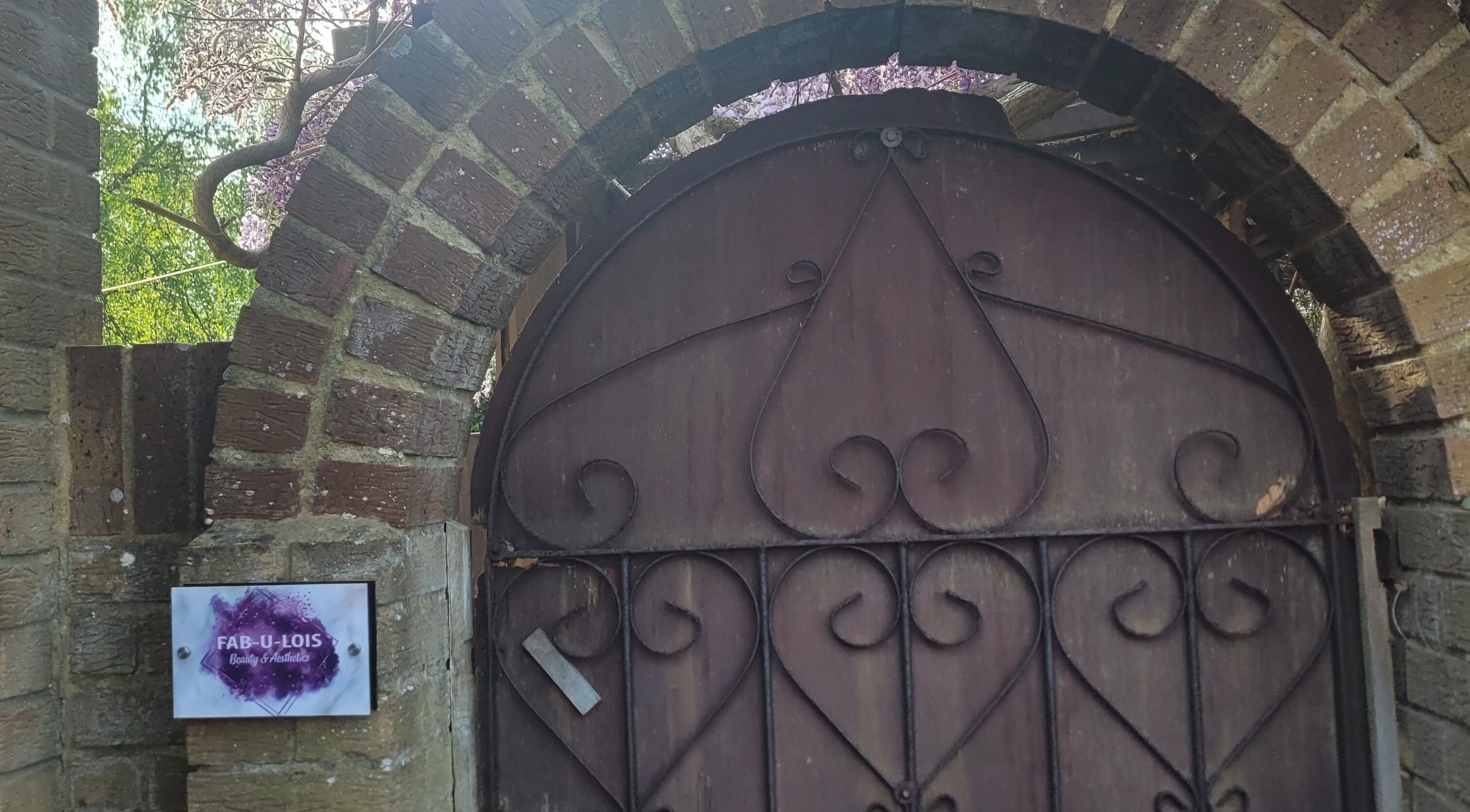 Rustic entry gate at Fab U Lois Beauty & Aesthetics in Rustington, England, GB, under a brick archway.