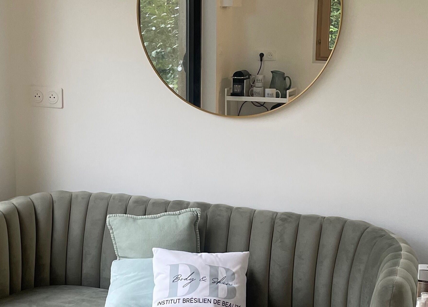 Espace détente élégant chez DB Body and Skin, Tresses, Nouvelle-Aquitaine, FR, avec canapé et miroir rond.