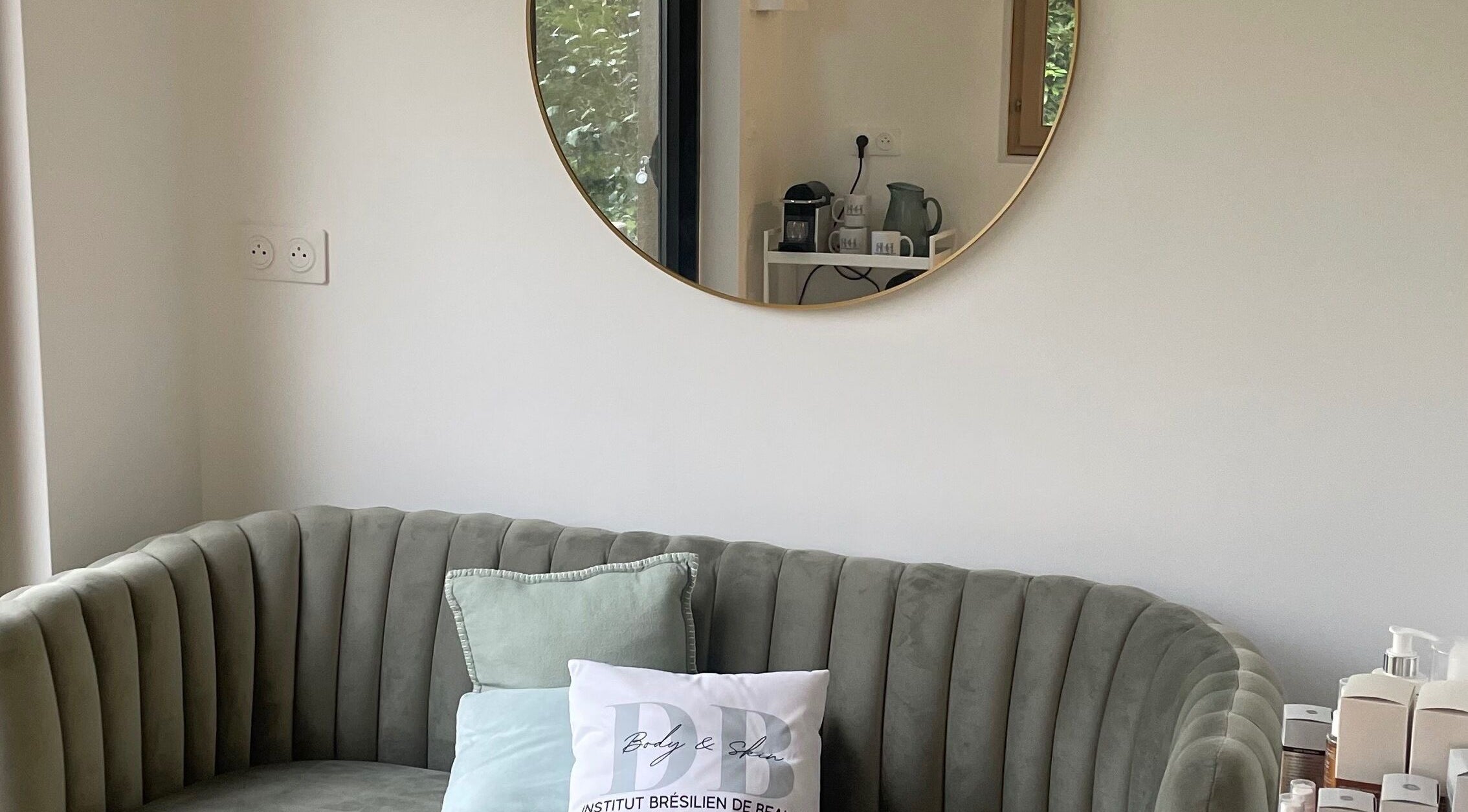 Espace détente élégant chez DB Body and Skin, Tresses, Nouvelle-Aquitaine, FR, avec canapé et miroir rond.