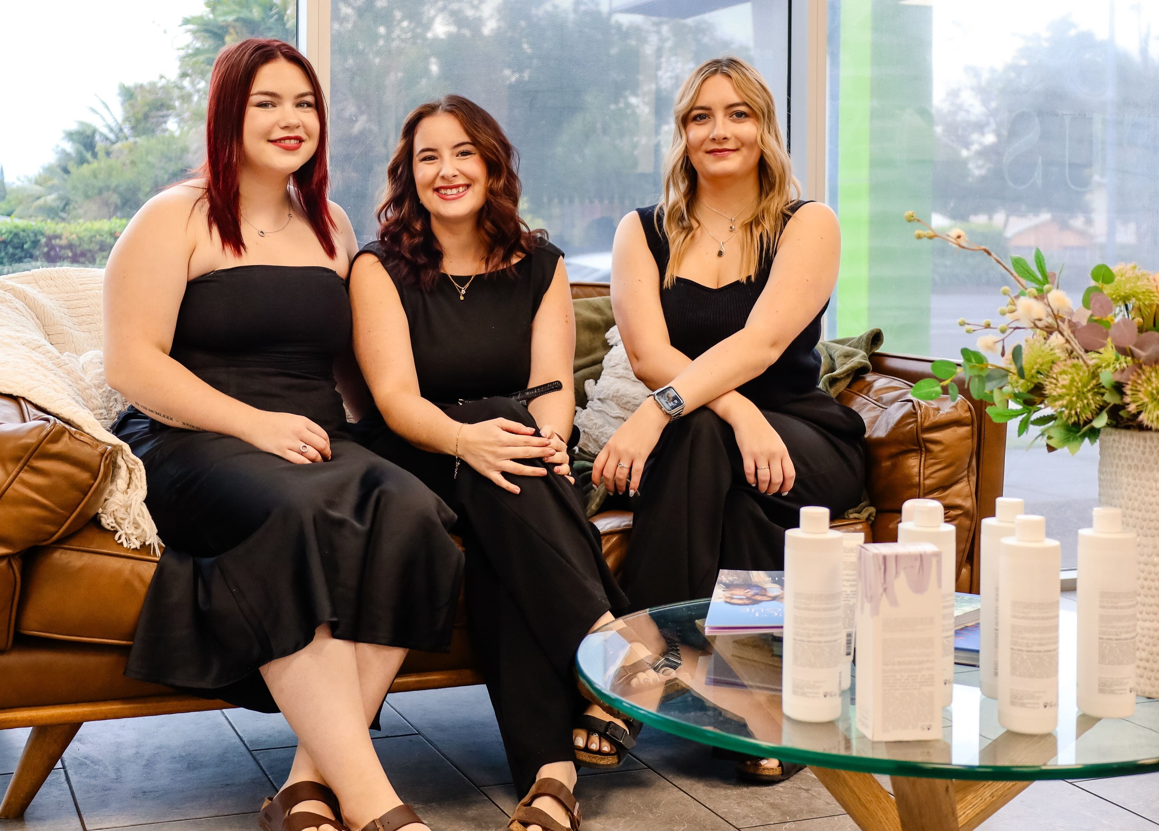 Team at Fusion Hair sitting on a sofa in Woree, Queensland, AU, surrounded by beauty products.