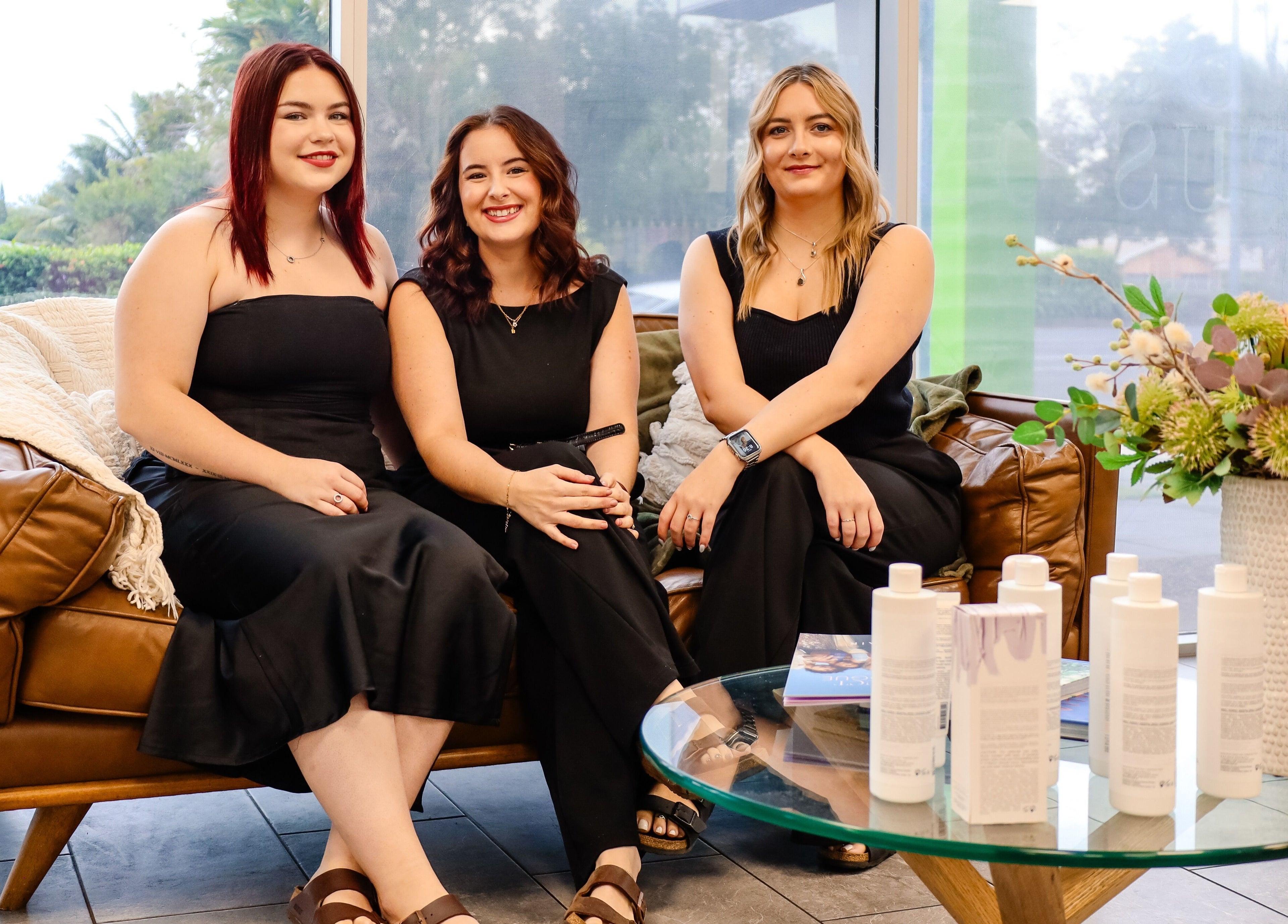 Team at Fusion Hair sitting on a sofa in Woree, Queensland, AU, surrounded by beauty products.