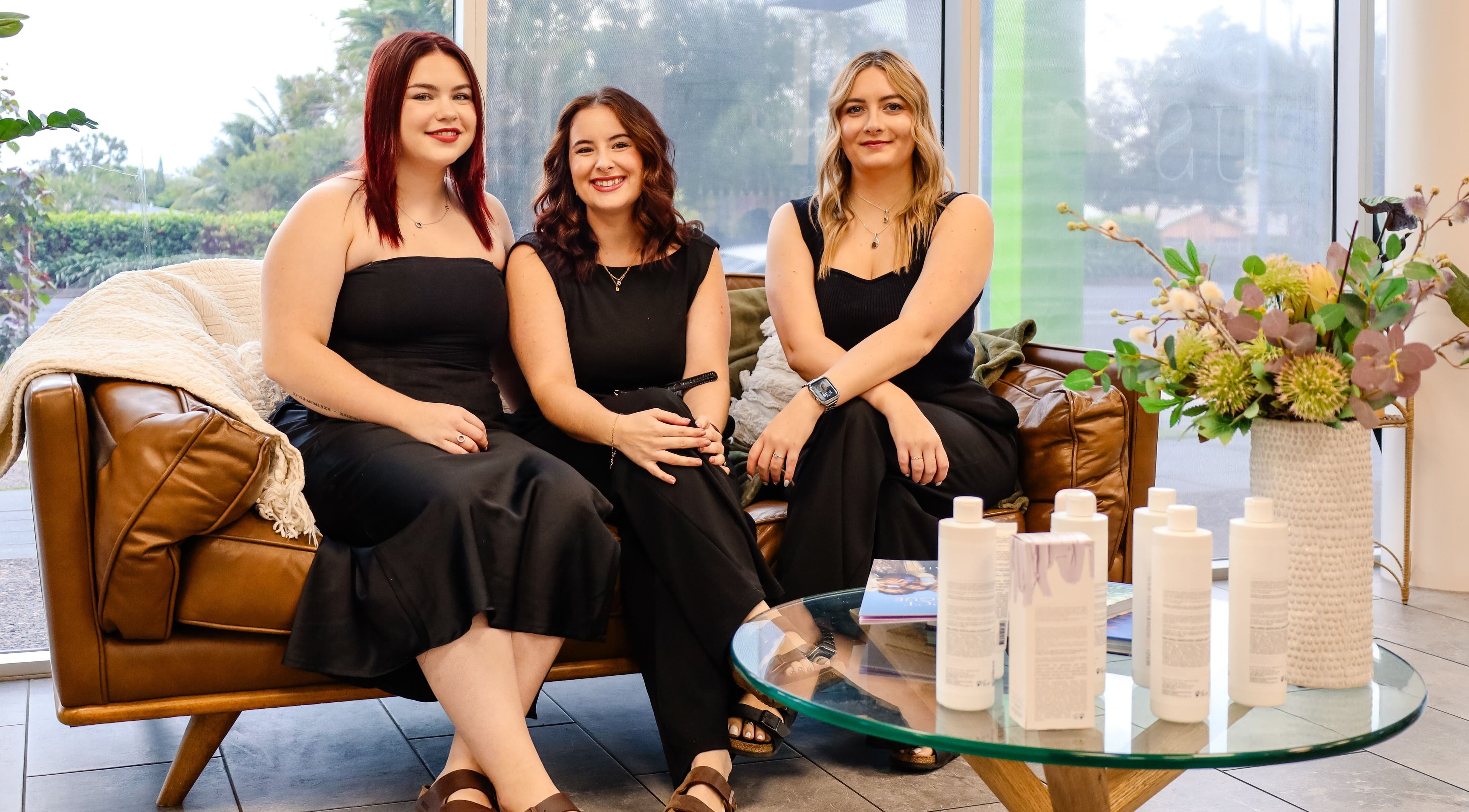 Team at Fusion Hair sitting on a sofa in Woree, Queensland, AU, surrounded by beauty products.