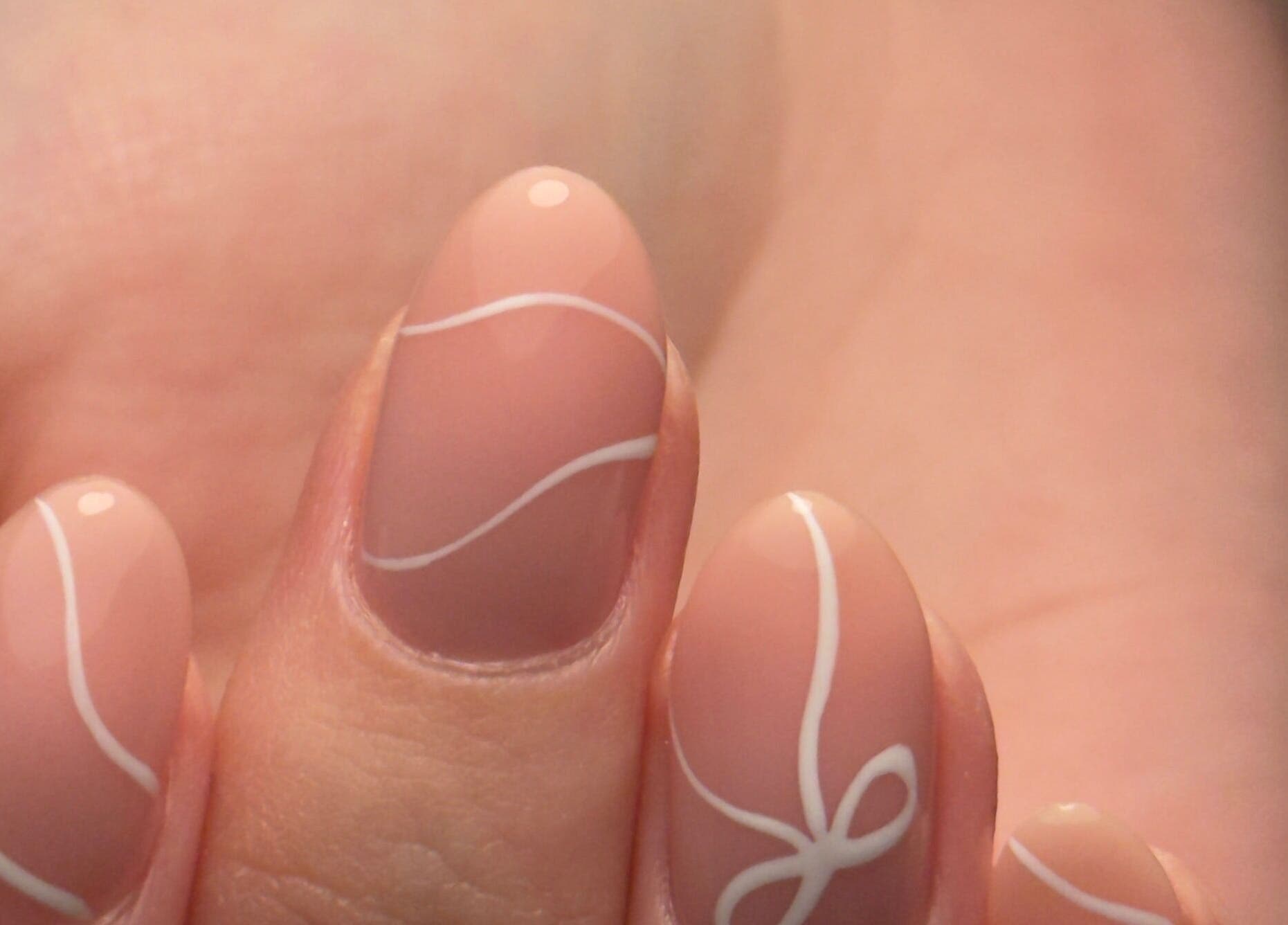 Close-up of chic nail art at Holly’s Beauty, Bridgwater, England, GB. Delicate white swirl designs on nude nails.
