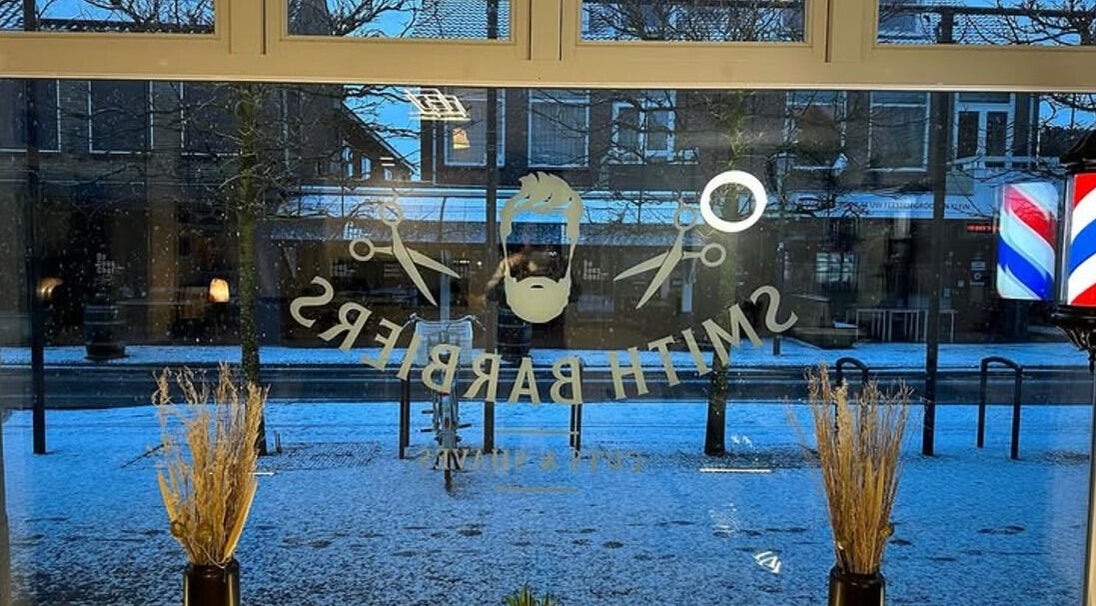 Uitzicht op besneeuwd straat vanaf Smith Barbiers in Woudenberg, Utrecht, NL met logo op raam.