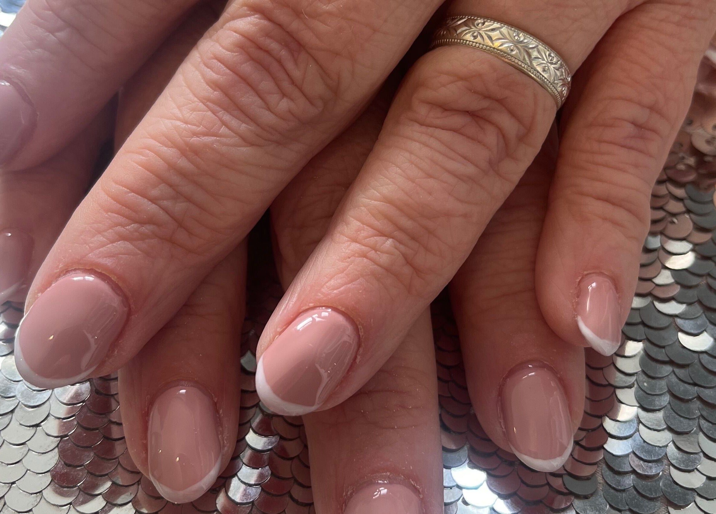 Manicured nails with a French tip design at Pretty Uneek at Home, Worthing, England, GB on sequin surface.