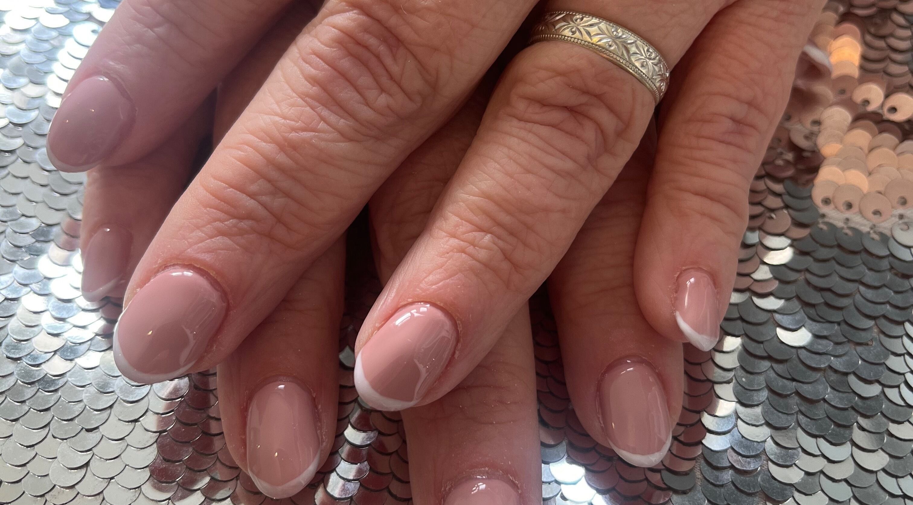 Manicured nails with a French tip design at Pretty Uneek at Home, Worthing, England, GB on sequin surface.