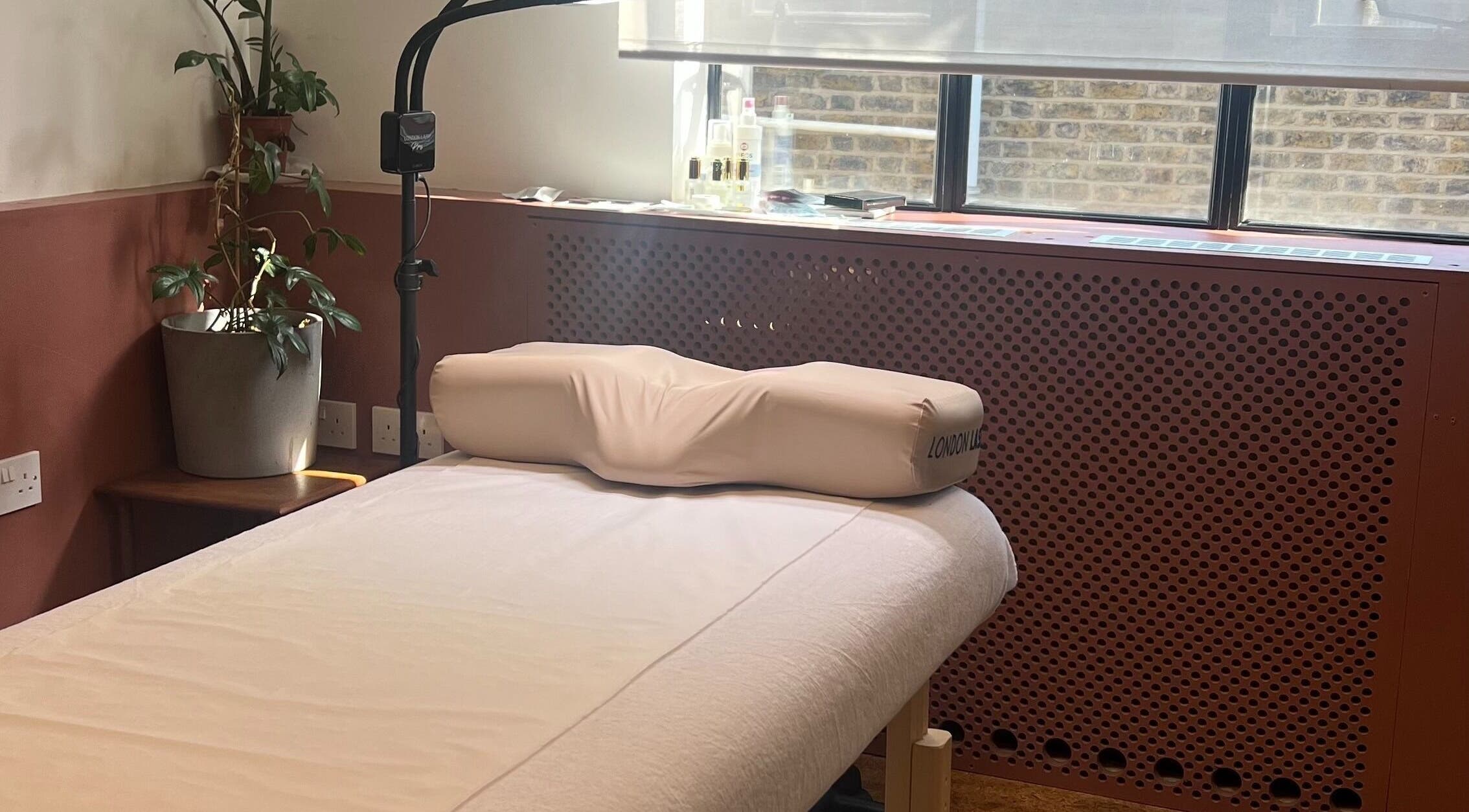 Calm treatment bed at Still Natural - Lash & Brow Styling, London, England, GB with natural light and plant.