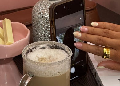 Manos con manicure en Mimo Beauty Center, Mérida, Yucatán, MX, junto a café espumoso y bombones.
