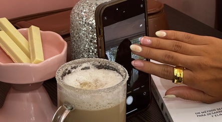 Manos con manicure en Mimo Beauty Center, Mérida, Yucatán, MX, junto a café espumoso y bombones.