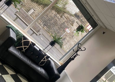 Cozy lounge area with black leather sofa at Ivy Hair & Beauty, Cowdenbeath, Scotland, GB.
