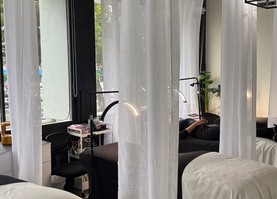 Área de relajación en Lumé Studio, Caguas, Caguas, PR con camillas y cortinas blancas.