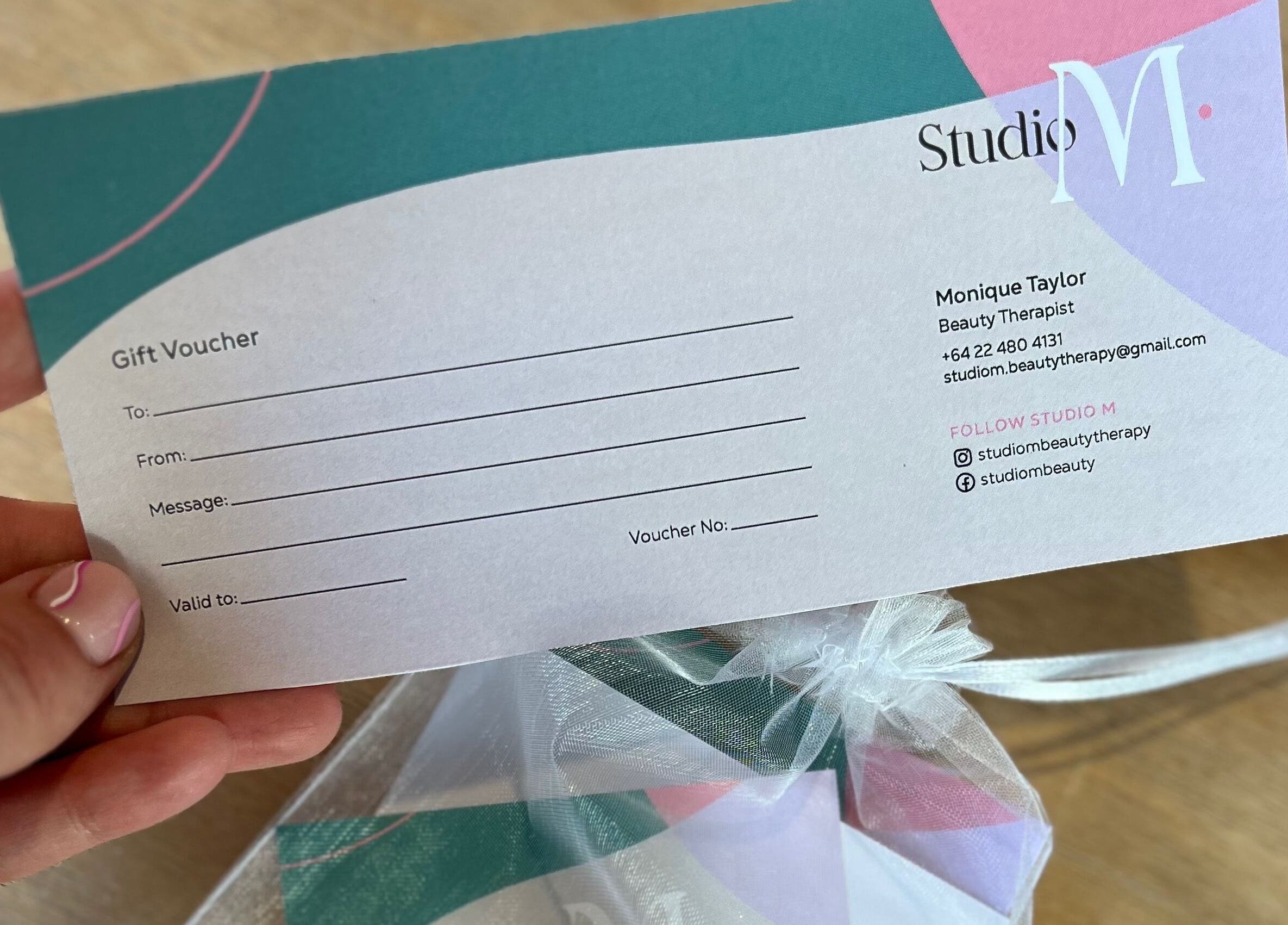 Studio M gift voucher held smilingly at Horsham Downs, Waikato, NZ, showcasing contact details.