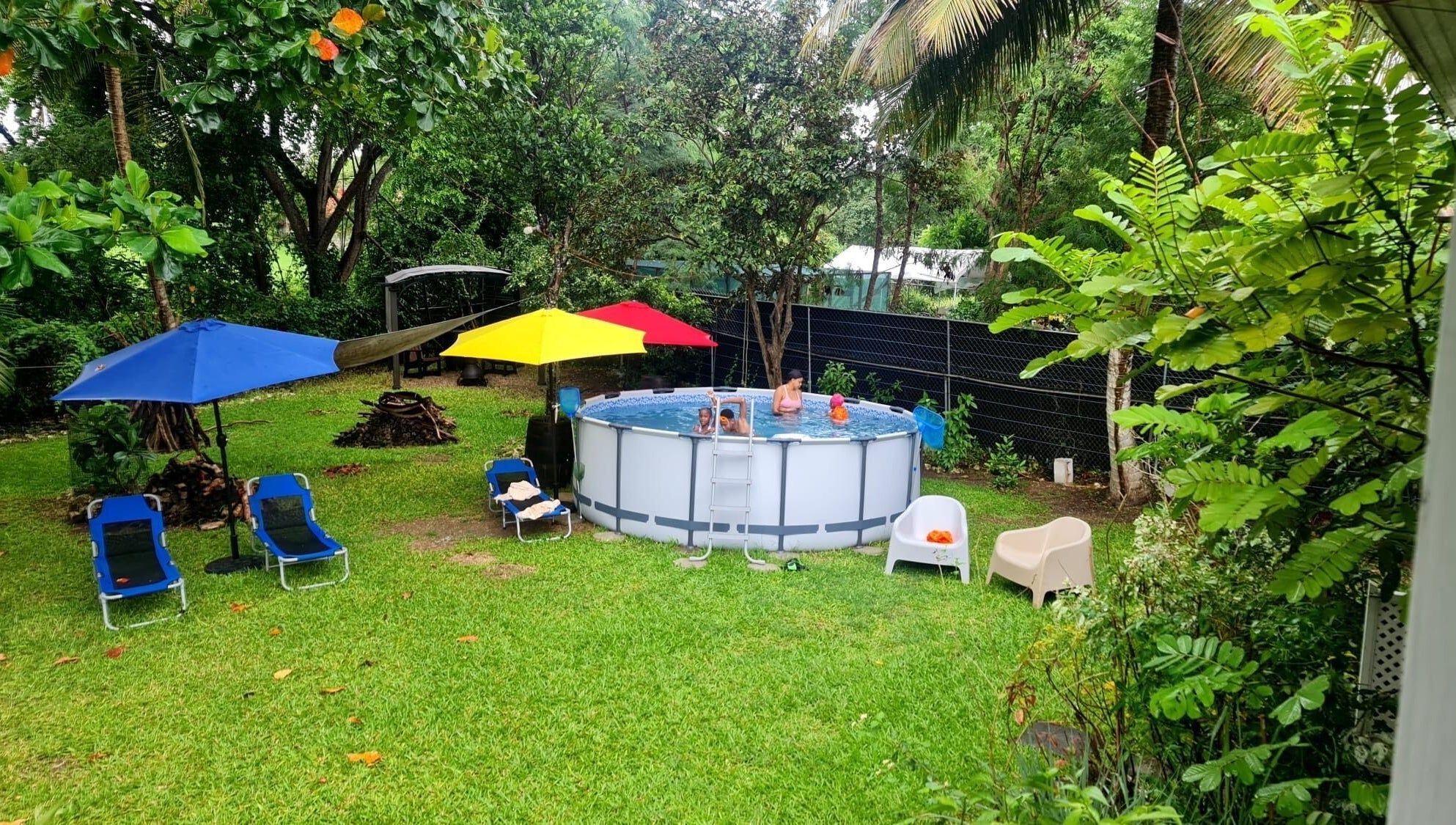 Outdoor pool area at Spa Holistic Health and Wellness, St. John, BB surrounded by lush greenery and umbrellas.