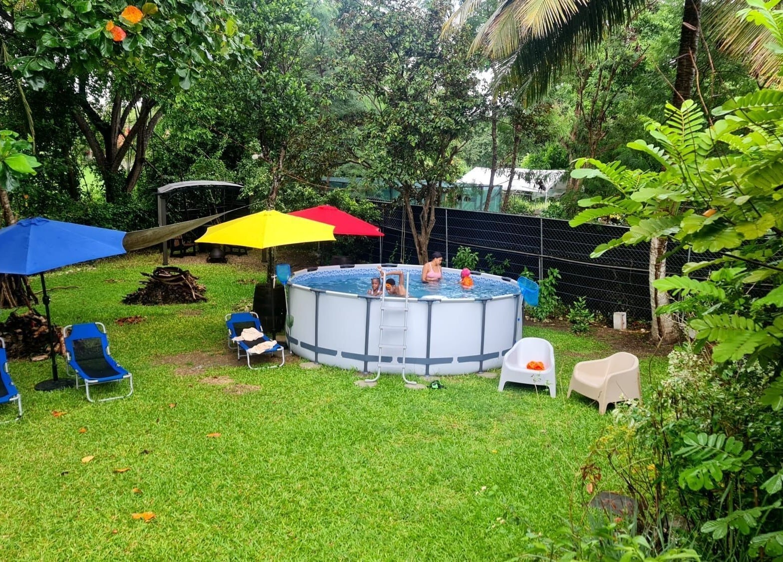 Outdoor pool area at Spa Holistic Health and Wellness, St. John, BB surrounded by lush greenery and umbrellas.