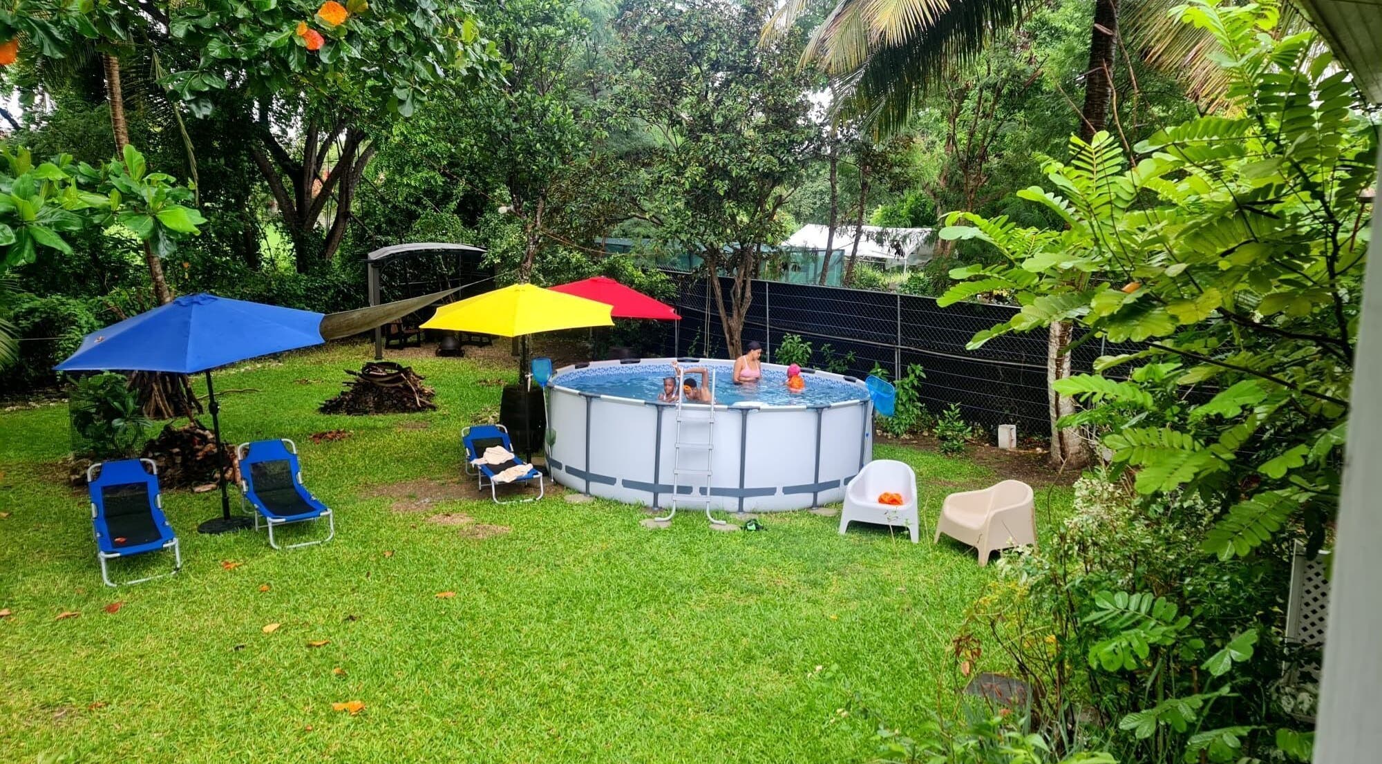 Outdoor pool area at Spa Holistic Health and Wellness, St. John, BB surrounded by lush greenery and umbrellas.