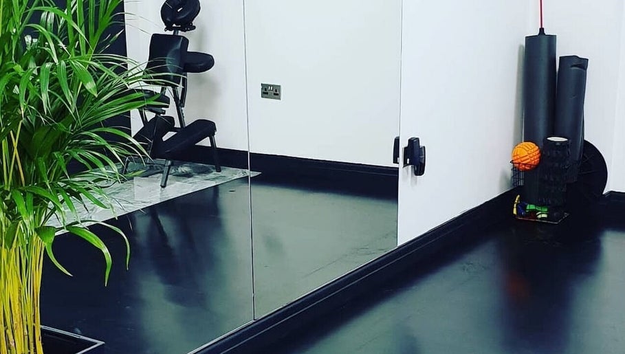 Modern therapy room at Optimum Physio, Birmingham, England, GB featuring a massage chair and lush indoor plant.
