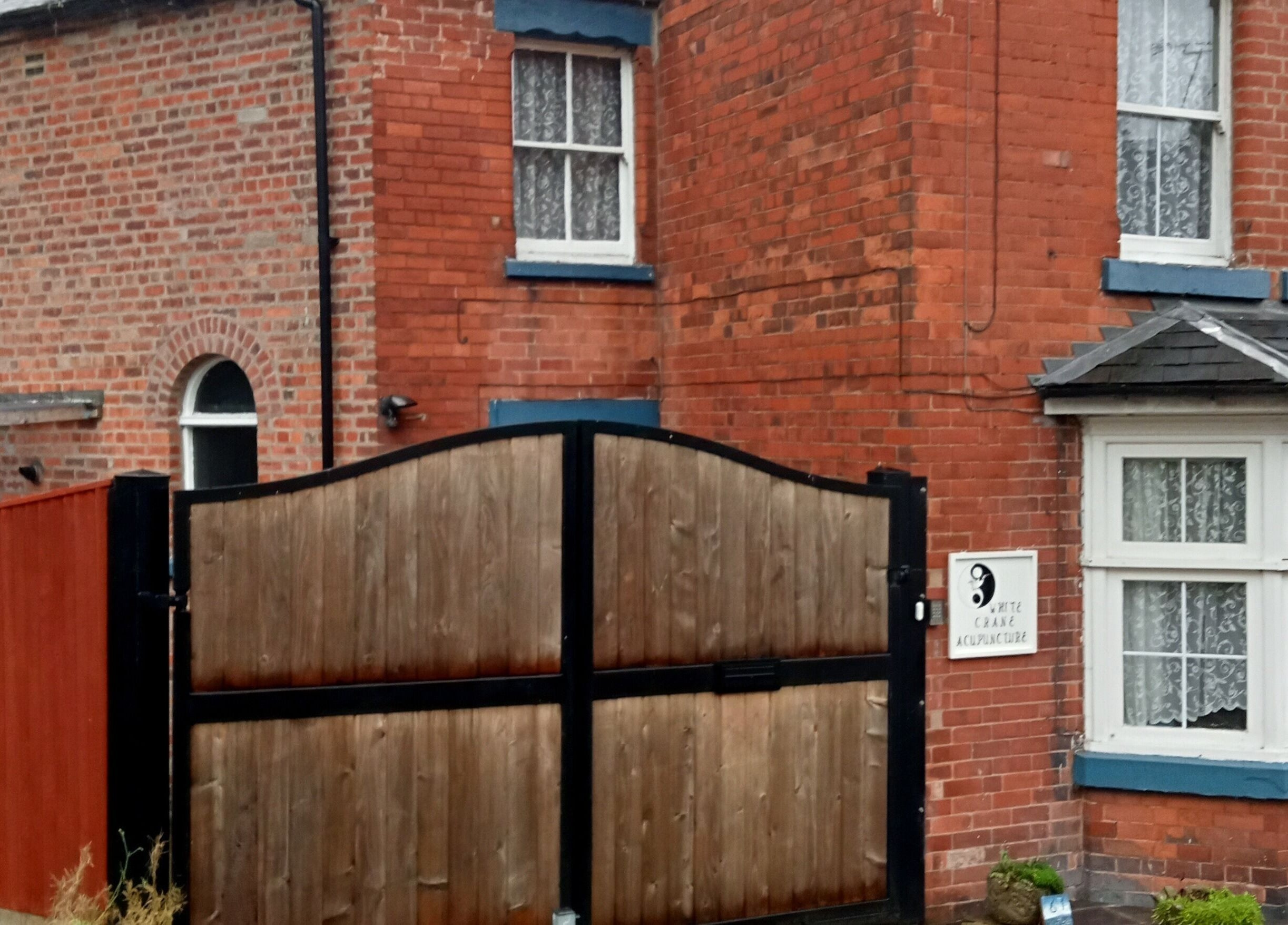 Front entrance of White Crane Acupuncture, Mansfield, GB, showcasing its charming redbrick exterior and gate.